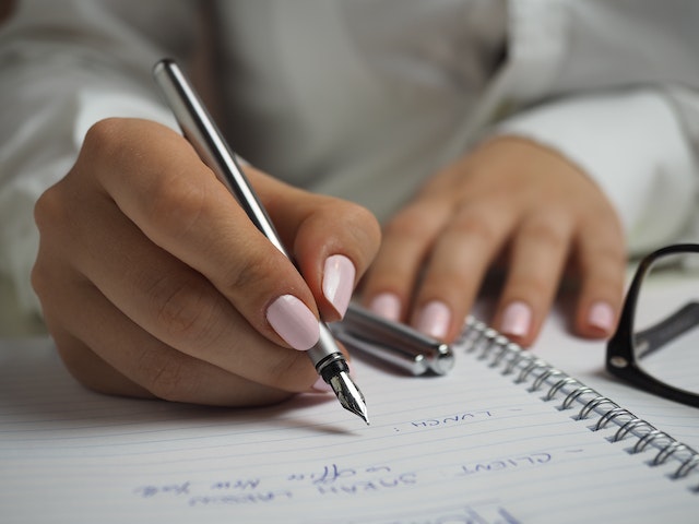person with pink nail polish writing in a journal